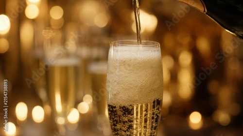 Close up of champagne being poured into glass with golden bokeh lights festive celebration