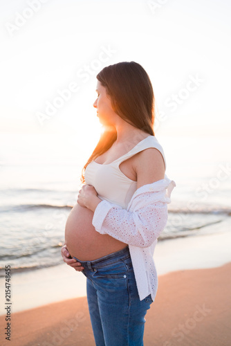 Quadro su tela Pregnant Woman Cradling Her Baby Bump on the Beach at Sunrise