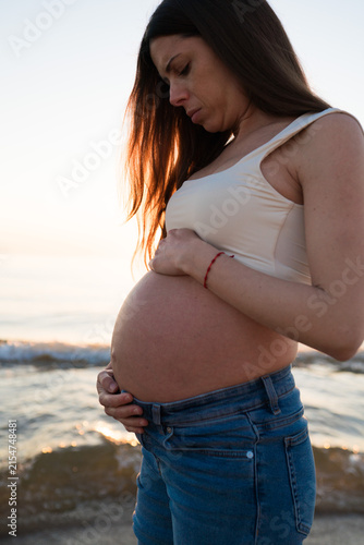 Foto Pregnant Woman Cradling Her Baby Bump on the Beach at Sunrise