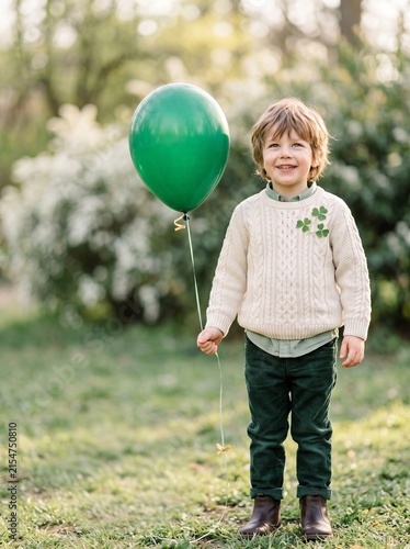 Happy child holding a green balloon in a sunny park on St. Patrick's Day  