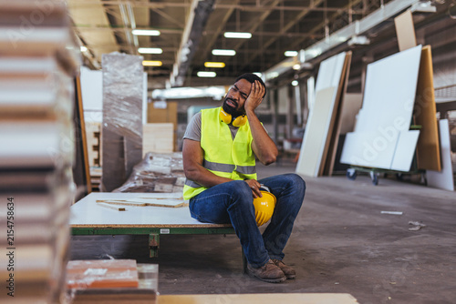 Foto Tired Construction Worker Sitting On Factory Floor Holding Hard Hat During Break