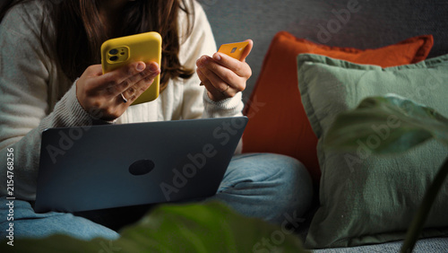 Anonymous young woman sitting on her sofa and shopping online while taking advantage of Cyber Monday deals, browsing discounts and making purchases from home.