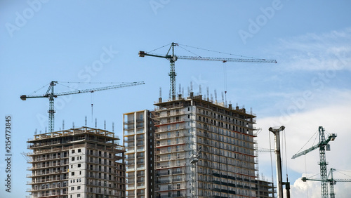 Photography Multiple green cranes are working on the construction of several tall concrete b