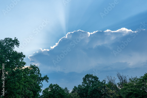 The sun is shining from behind the cloud in the  sky.
