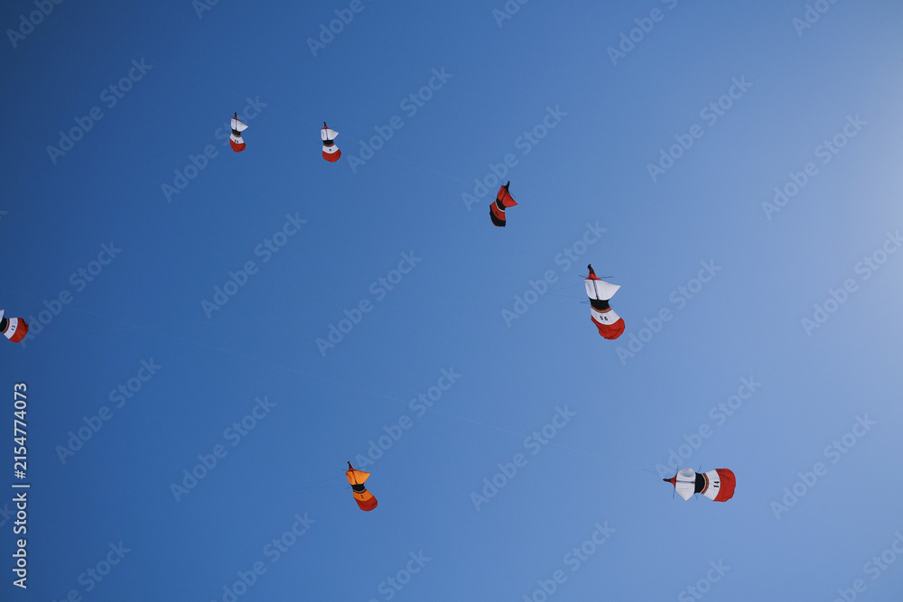 Fototapeta premium Colorful traditional Balinese kites flying in a blue sky with sunlit kite strings