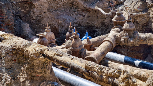 Bild auf Leinwand Old, corroded cast iron pipes and valves are exposed in a trench, revealing a co
