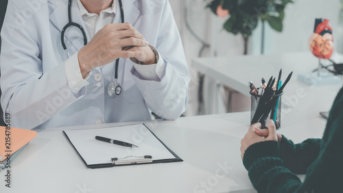 A male doctor is listening to and counseling an Asian female patient at his desk in a clinic during a health check-up.