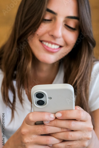 Smiling young woman looking at smartphone while texting, relaxed and happy, close-up of hands and mobile device showing everyday technology, communication and social media use