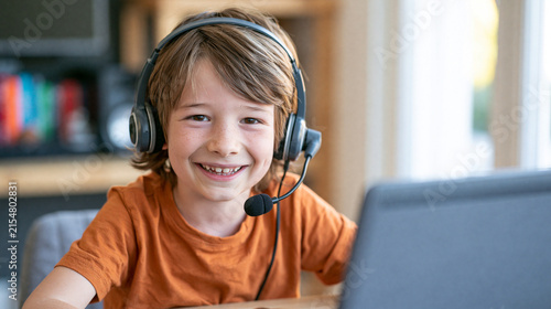 Smiling young boy wearing modern black gaming headphones while using laptop computer on white background