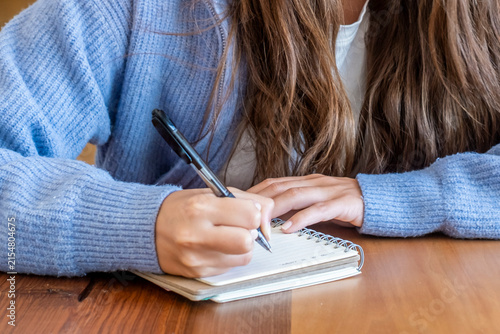 Photography Young student writing notes in a spiral notebook on a wooden table, focused and