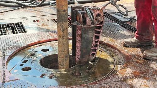 An oilfield worker is setting drillpipe slip equipment and handling drill pipes on a rig floor during exploration. Heavy industrial working scene, close-up.