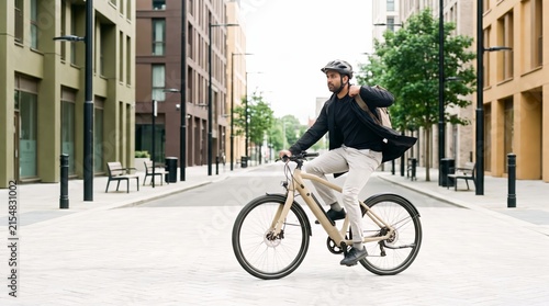 Man in business clothes commuting to work on an electric bike on a sunny city street