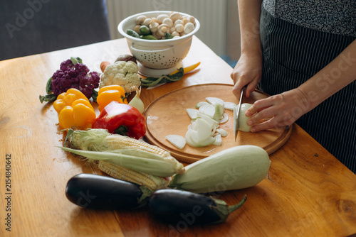 Person chopping onion on wooden cutting board with vegetables