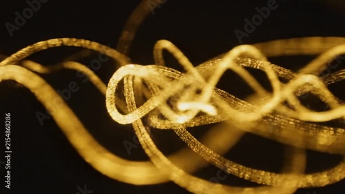 Abstract golden light trails drawing elegant looping spiral shapes with dark background