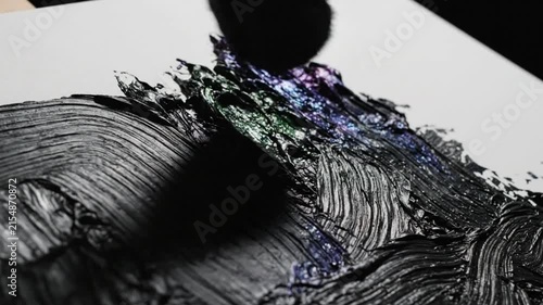 Close up view of artist applying layered black iridescent paint strokes on white canvas, abstract texture detail