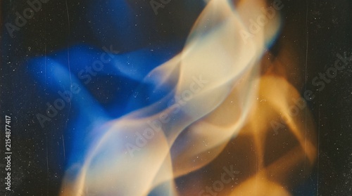 Abstract image of swirling blue and golden flames or smoke against a dark, textured background.