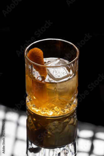 Close up of a classic old fashioned cocktail on a dark reflective background garnished with an orange twist.