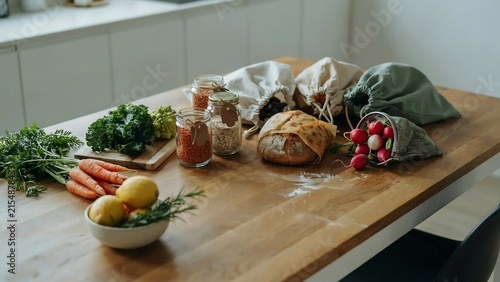 Fresh vegetables and artisan bread in reusable cotton bags on wooden kitchen table
