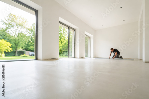 Un trabajador coloca el piso en una sala vacía con ventanas grandes y vista al jardín