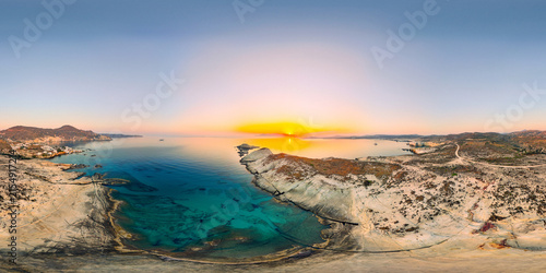 Sunrise over Mandrakia on Milos paints the sky in gold and orange hues above turquoise water and rugged coastal cliffs, revealing the tranquil beauty of the Aegean Sea.