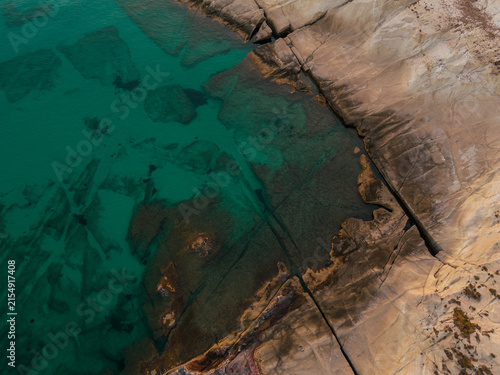 Aerial view of turquoise water and smooth rocky shoreline near Sarakiniko Beach on Milos, revealing unique geological patterns and the vivid colors of the Aegean Sea.