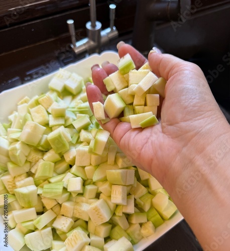 Hand holding diced green vegetables above a bowl in kitchen  