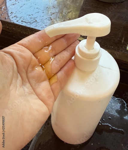 Pump bottle dispensing liquid onto hand over wet surface  