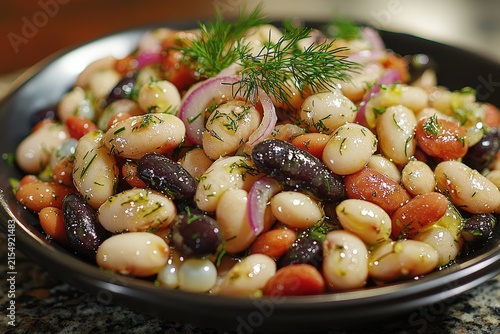 Colorful bean salad with fresh herbs, red onion, and olive oil in a black bowl on a granite surface
