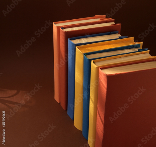 Books with colorful paper covers are lined up against colorful paper backgrounds. School education featuring attractive, bright, and colorful books.