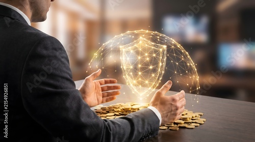 A businessman framing his hands around a glowing golden digital dome and shield protecting gold coins.