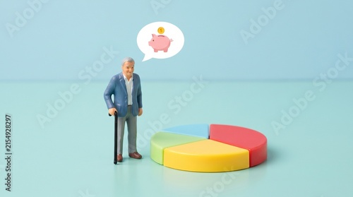 Miniature senior man standing next to a colorful pie chart thinking about his piggy bank savings for retirement