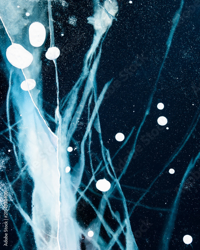 Transparent blue ice with cracks on Baikal lake in winter. Abstract winter nature background.