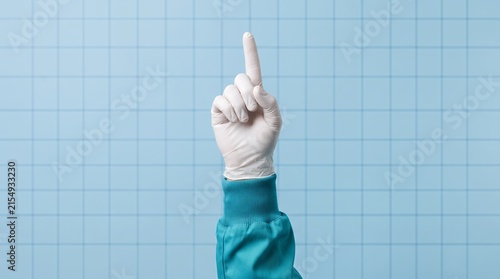 A medical professional's hand wearing a white glove points its index finger upwards against a tiled blue background.