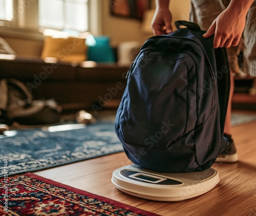 Person Weighing Backpack on Digital Scale in Living Room
