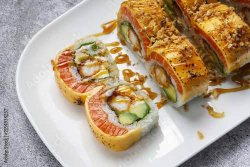 Salmon sushi rolls with tempura shrimp, avocado and torched cheese on white plate. Delicious fusion sushi rolls topped with seared cheddar cheese and salmon fish slices
