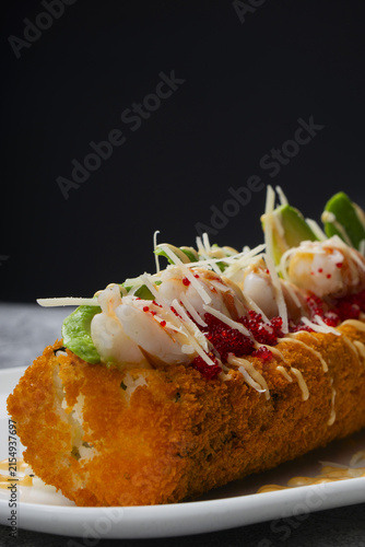 Crispy sushi hot dog roll fried in panko breadcrumbs topped with shrimp, avocado and red caviar. Fusion Japanese food crunchy tempura sushi dog with seafood tartar, red tobiko and spicy sauce.