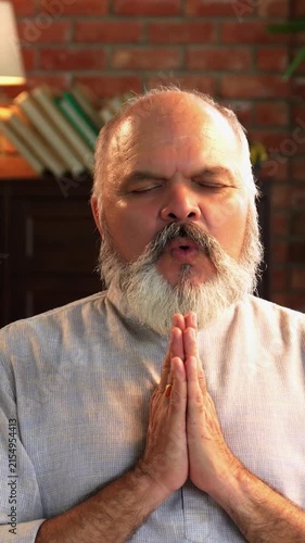 An Indian Asian elderly dressed in traditional Indian clothes and is chanting 'OM' with his hands folded and eyes closed, in a peaceful environment