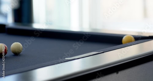 Cue striking cue ball and guiding yellow ball into corner pocket, players celebrating near windows