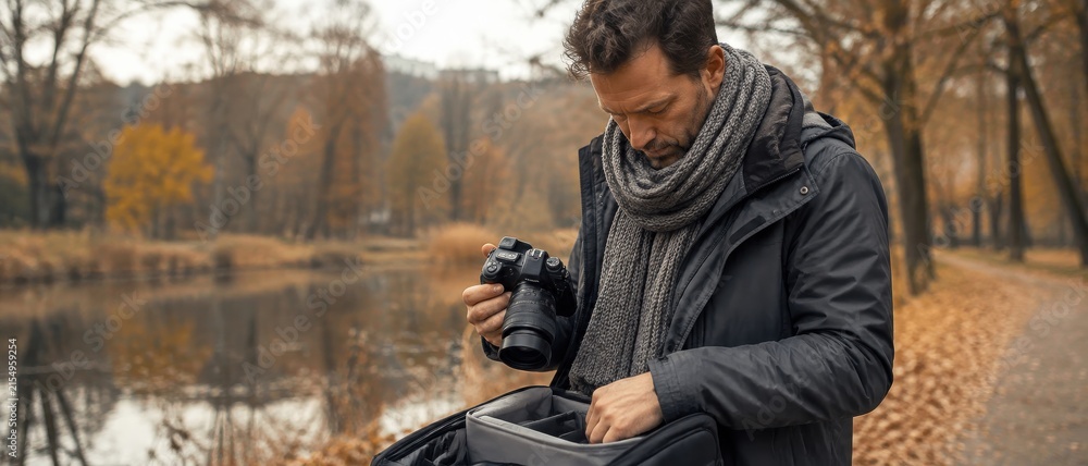 Obraz premium Man in warm scarf and jacket prepares camera for outdoor autumn photography