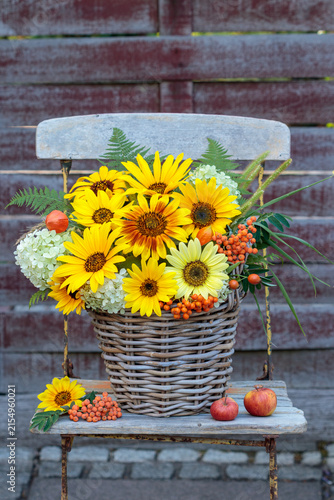 Blumenstrauß mit Sonnenblumen, Rispenhortensie, Vogelbeeren, Farnblättern und Gräsern im Korb auf einem Gartenstuhl