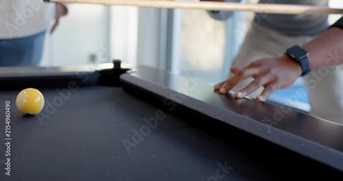 Diverse male friends playing pool, drawing cue and striking cue ball, then laughing by windows