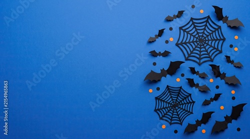 Top view of halloween decorations with black paper bats and spider webs arranged on a vibrant blue background surface