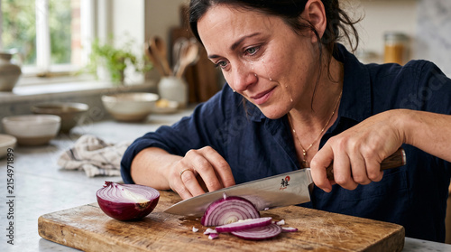Woman slicing red onion with a knife in a bright kitchen  