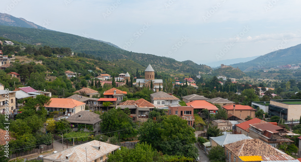 Fototapeta premium Scenic landscape of Mtskheta with a historic church, red-roofed houses, and mountain ranges