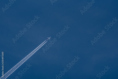 Commercial airplane flying high in the clear blue sky leaving a long white contrail vacation travel holiday