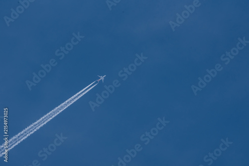 Commercial airplane flying high in the clear blue sky leaving a long white contrail vacation travel holiday