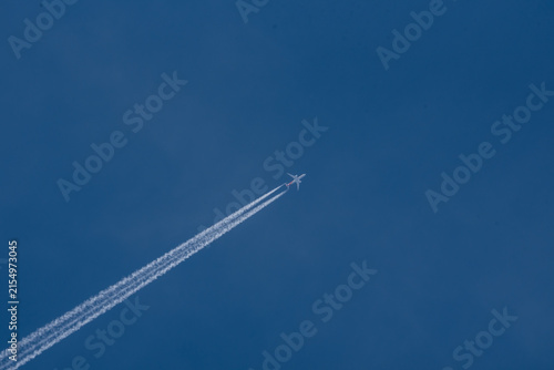 Commercial airplane flying high in the clear blue sky leaving a long white contrail vacation travel holiday