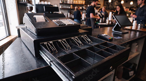 Cash register drawer open in a busy coffee shop with staff serving customers  