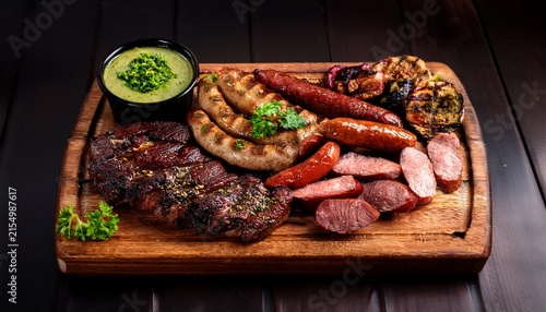 asado with assorted grilled cuts and chorizo served with chimichurri on wooden board