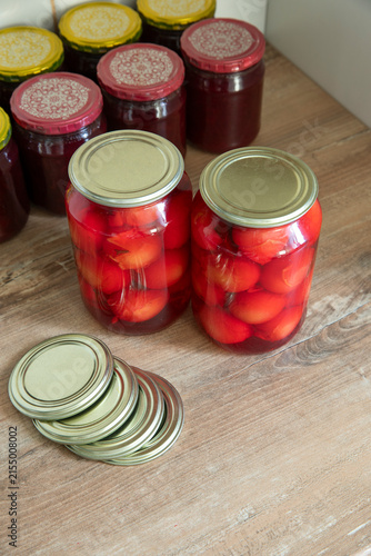 Homemade canned preserves in glass jars with metal lids and additional canning lids on a wooden table, traditional food preservation concept.